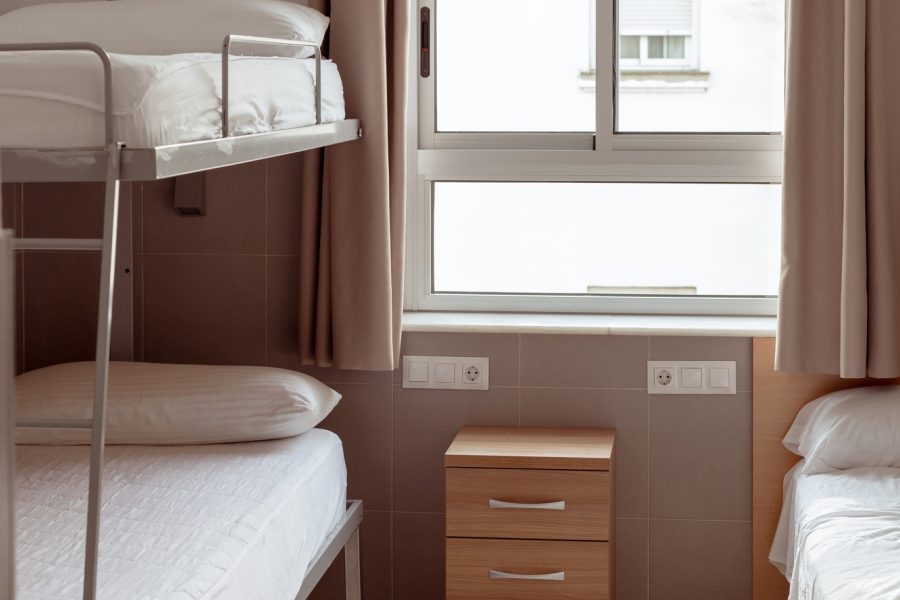 A clean and minimalistic hostel room with a bunk bed, white bedding, and small wooden bedside table